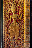 Wat Xieng Thong temple in Luang Prabang, Laos. Detail of a wooden door of the sim with gilded carvings on a red background. 